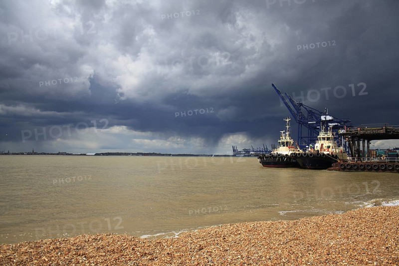 Tugboats moored at harbour of container port with passing rainclouds