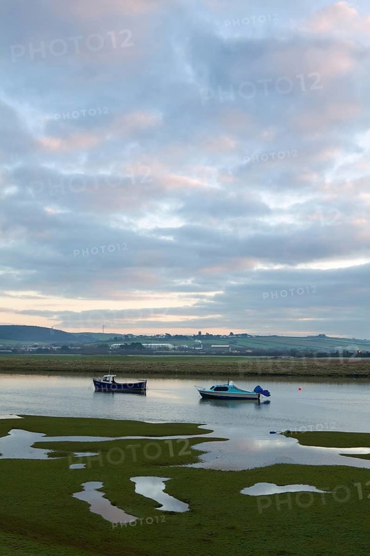 Two small boats rising with incoming tide on tidal stretch of river at dawn