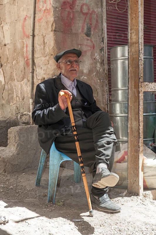 Old man with a walking stick seated on a plastic chair