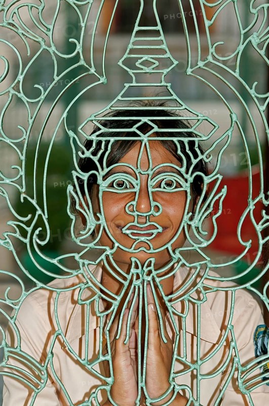 Young Khmer woman looking through a metal lattice gate with a Buddha figure