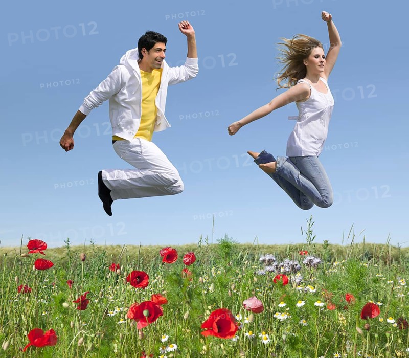 Young couple jumping over a flower meadow in early summer