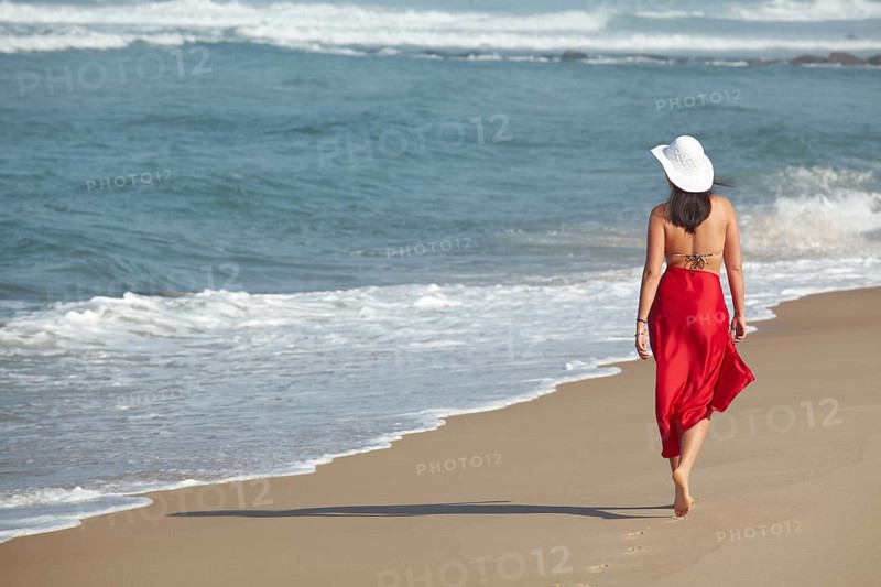 Rear view of a young woman wearing a bikini and a red sarong walking along a beach in summer