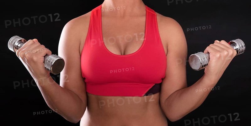Young woman's upper body wearing a red sports bra while doing fitness training with chrome dumbbells