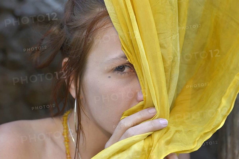 Young woman hiding behind a yellow silk scarf