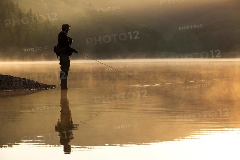 A fly fisherman standing on the shore of the Obernau reservoir at sunrise