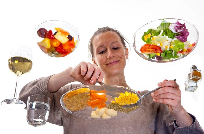 Young woman sitting at a glass table eating steak with vegetables and potatoes