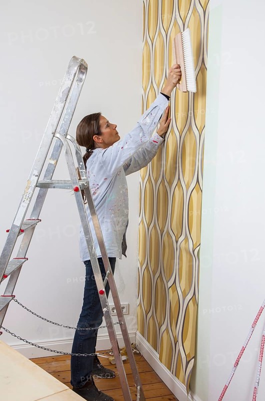 Young woman wallpapering a wall