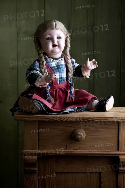 Antique doll sitting on a small chest of drawers