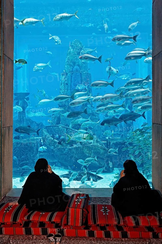 Two Arab women talking on their cell phones in front of an aquarium in The Lost Chambers
