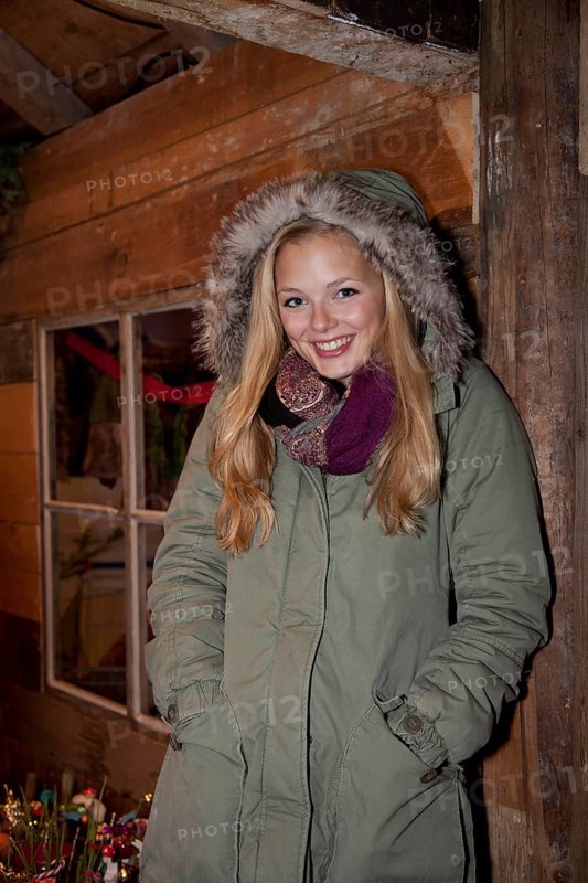 Smiling young woman wearing a green parka standing in front of a hiking hut decorated for Christmas