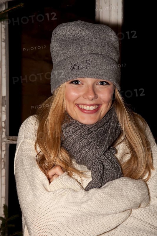 Smiling young woman wearing a cap and a scarf standing in front of a hiking hut