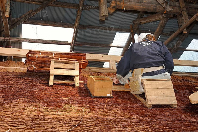 A roofer with a hard hat is nailing cypress bark to the roof of the Kamigamo Shrine