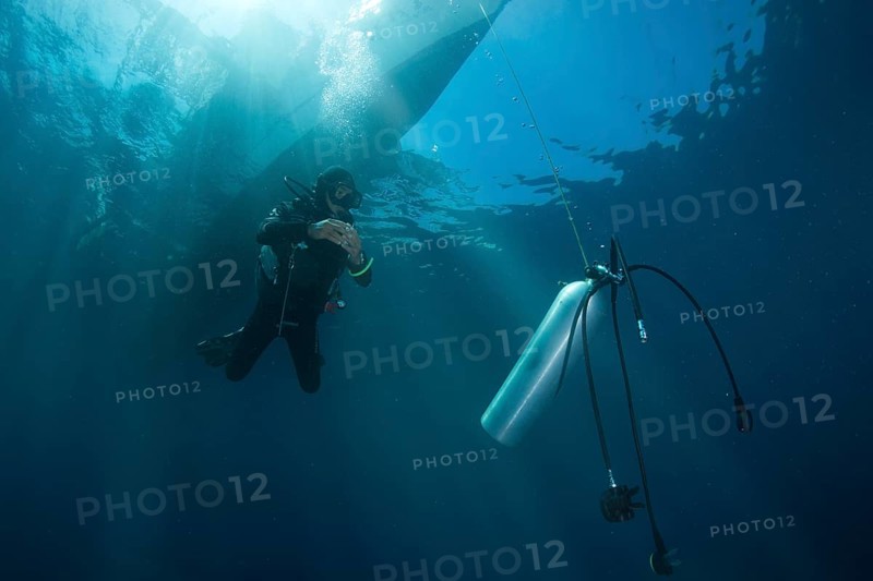 Diver with spare air tank during a decompression stop under a boat