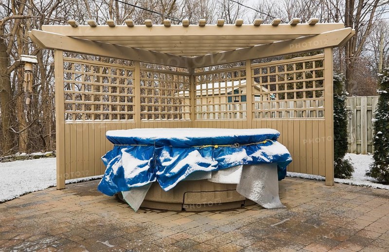 Wooden pergola and a spa in a residential backyard covered up for the winter season