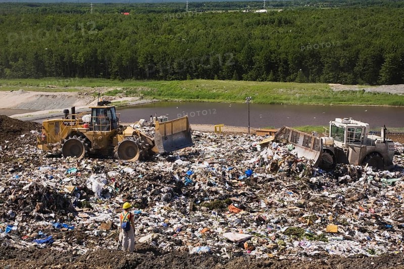 Heavy machinery spreading out and compacting discarded debris and trash at a waste management site