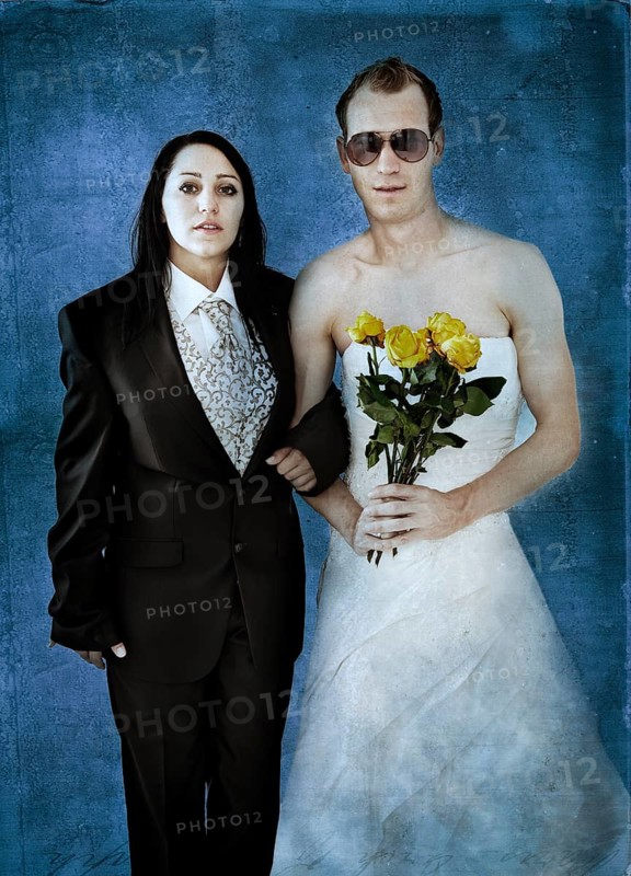 Bride wearing a suit and a groom wearing a wedding dress with sunglasses and yellow roses