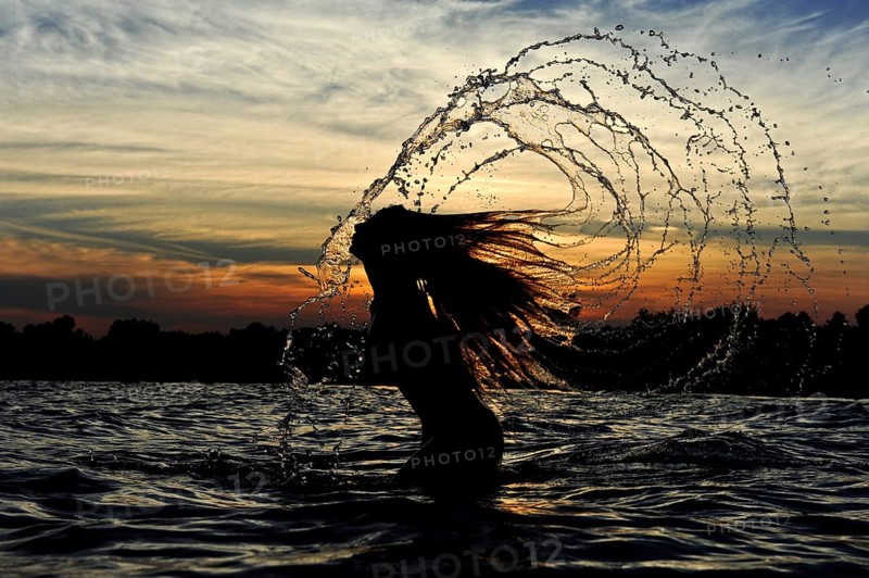 Young woman standing in the sea throwing back her long hair with splashing water