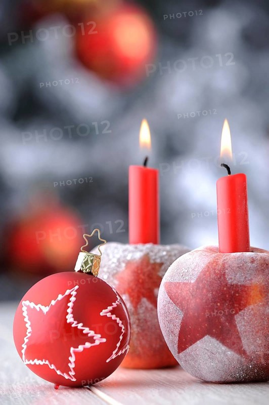 Red Christmas bauble with apples and candles in front of a Christmas tree