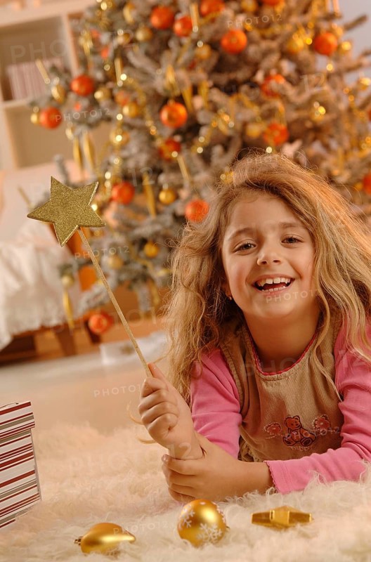 Smiling girl lying on the ground with a golden star and gifts in front of a Christmas tree