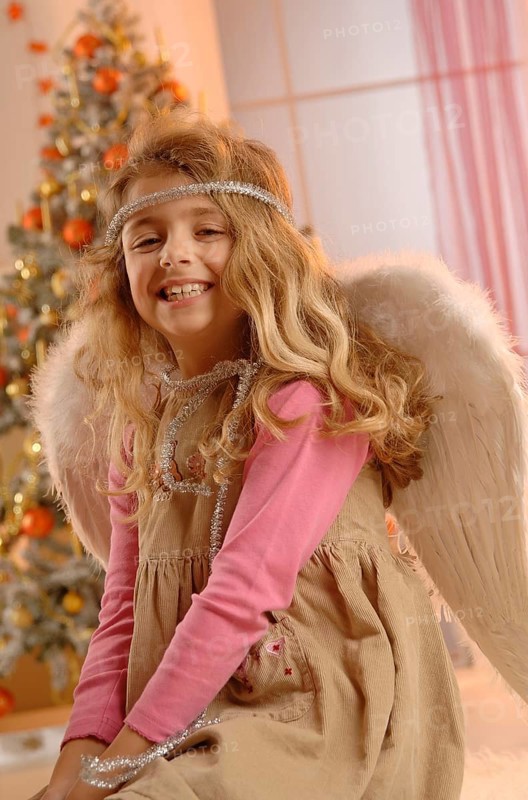 Smiling girl wearing a dress with angel wings in front of a Christmas tree