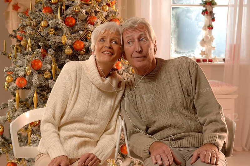 Mature couple with headphones sitting in front of a Christmas tree