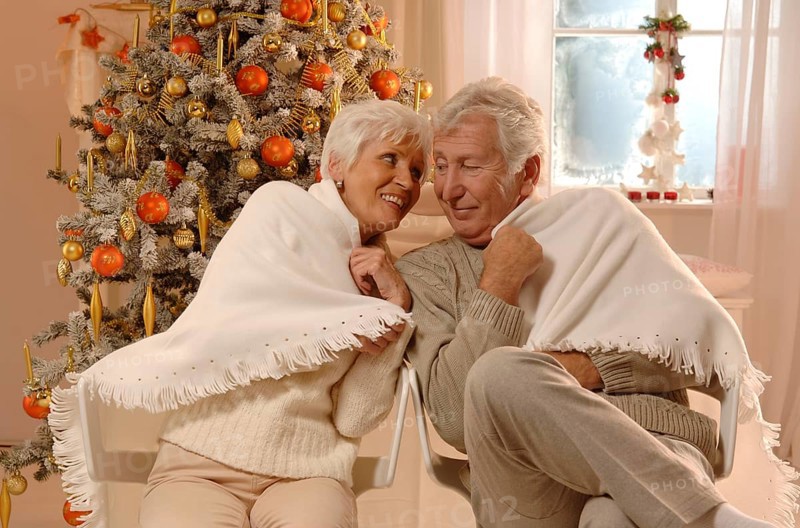 Mature couple in love wrapped in a blanked sitting in front of a Christmas tree