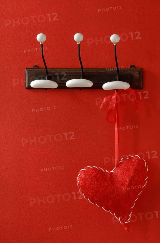 Red fabric heart hanging from nostalgic clothes hooks on a red wall