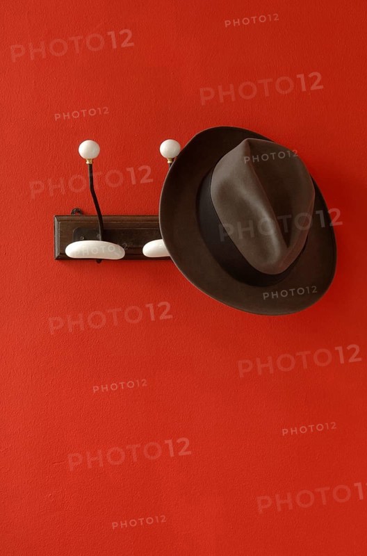 A man's hat is hanging on nostalgic clothes hooks on a red wall