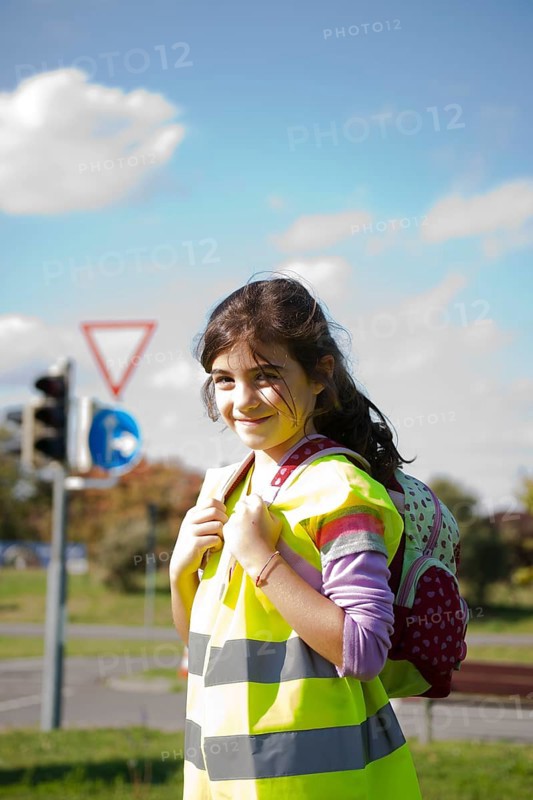 Girl with a school bag wearing a safety vest in front of a road sign