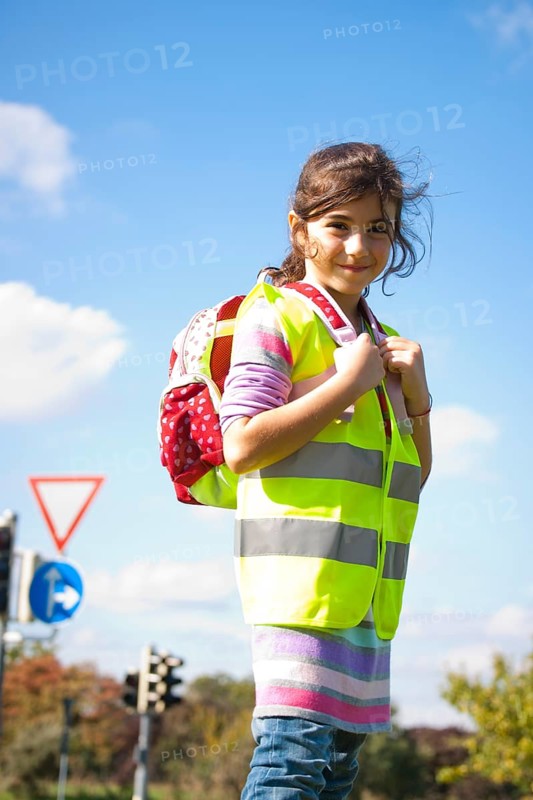 Girl with a school bag wearing a safety vest in front of a road sign