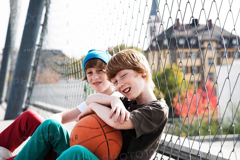 Two cool boys sitting with a basketball on a playground