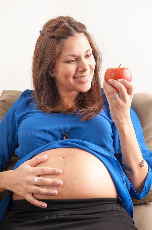 Pregnant woman holding hand on her stomach and eating an apple