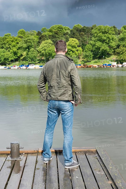 Man standing on jetty by a lake and looking at rainclouds
