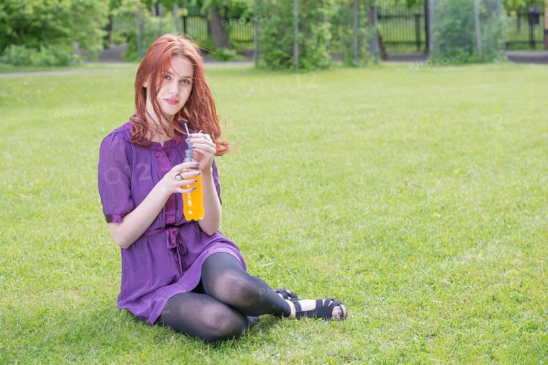 Young woman sitting in a park with a bottle of orange soda