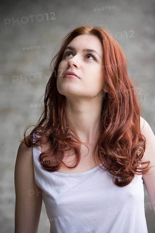 Pensive young woman with red hair looking up