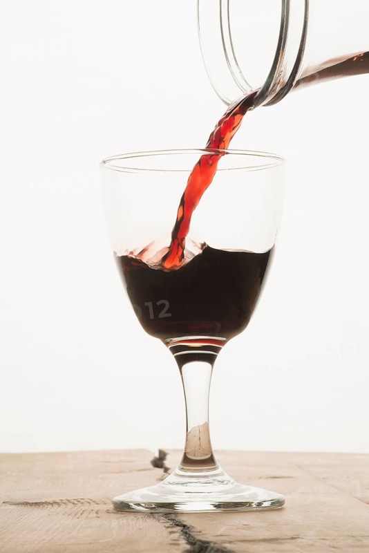 A glass of red wine being filled from a carafe