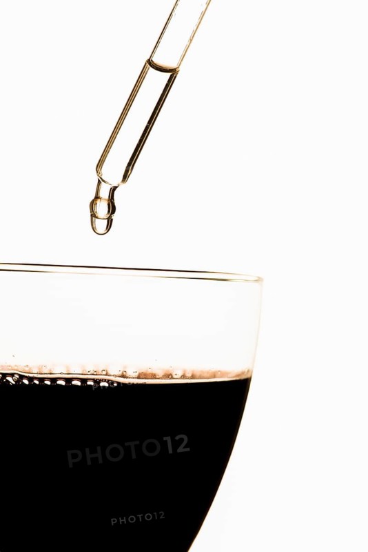 Pipette putting toxic substance in glass filled with red wine