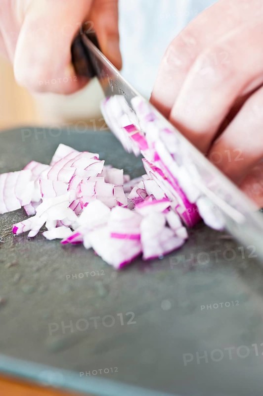 Red onion being cut on a plastic cutting board