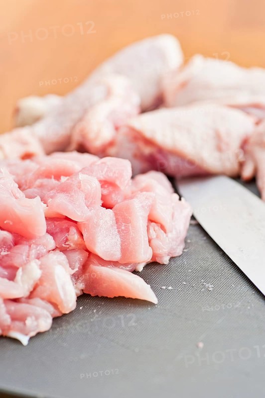 Cut up pieces of uncooked chicken on a plastic cutting board