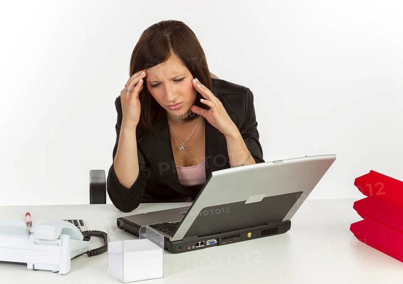 Young woman with a headache sitting at a desk with a laptop