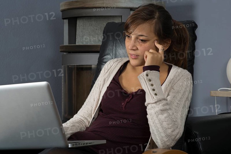 A young woman of Indonesian origin is sitting in front of a wood burner working on a laptop computer