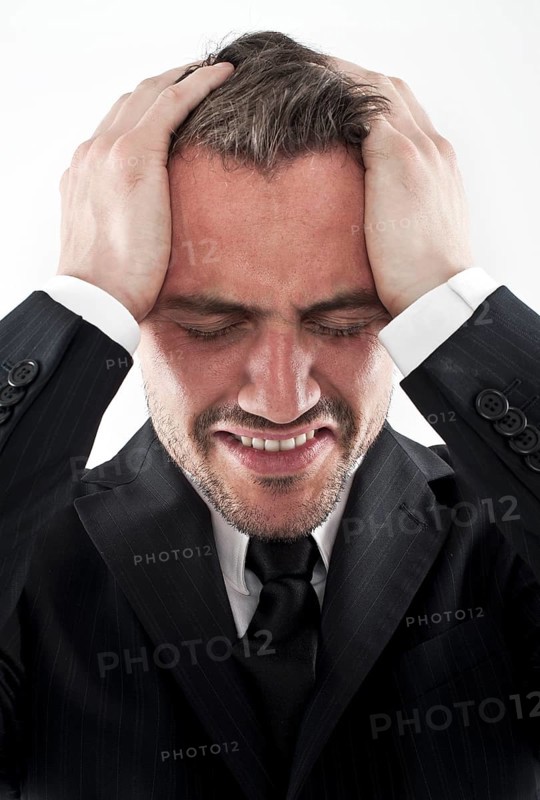Desperate young man wearing a suit holding his hands to his face