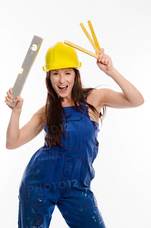 Woman wearing blue overalls and a hardhat holding a folding carpenter's ruler and a spirit level