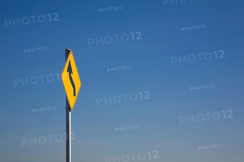 Yellow traffic sign with a curved black 'S' arrow against a blue sky
