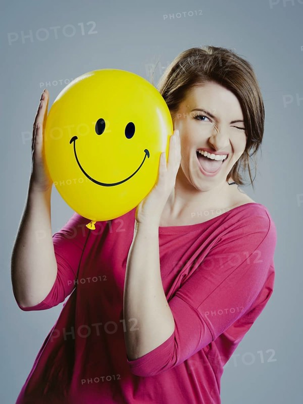 Smiling young woman holding a smiley face balloon