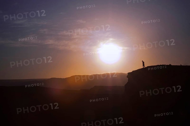Man standing on the edge of a cliff at sunset