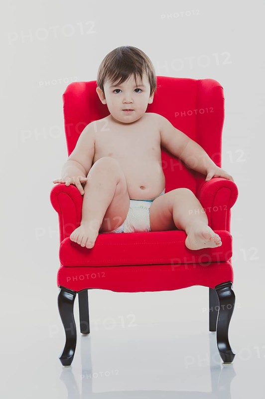 Young boy wearing a diaper sitting on a red chair