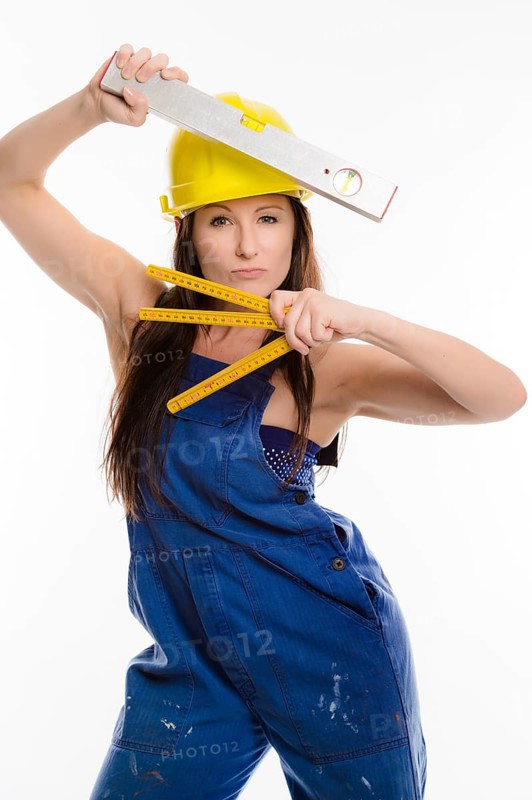 Woman wearing blue overalls and a hardhat holding a folding carpenter's ruler and a spirit level