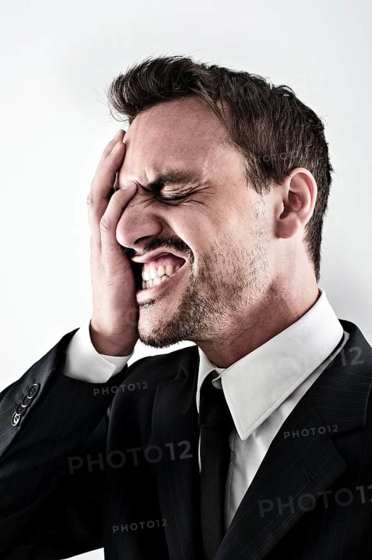 Desperate young man wearing a suit covering his face with his hand