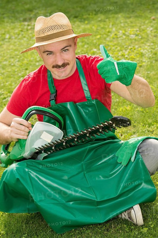 Gardener holding a hedge trimmer while sitting on the lawn